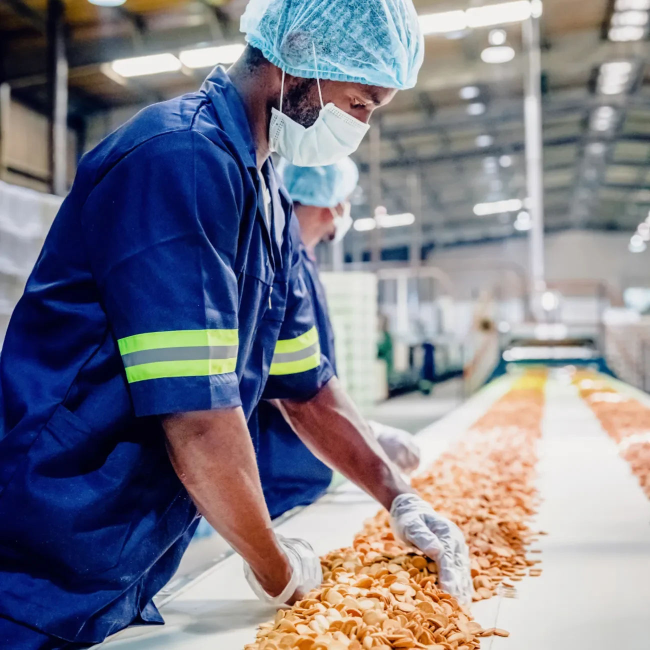 Mitarbeiter in Schutzkleidung kontrollieren Produkte am Fließband im Lebensmittelbetrieb