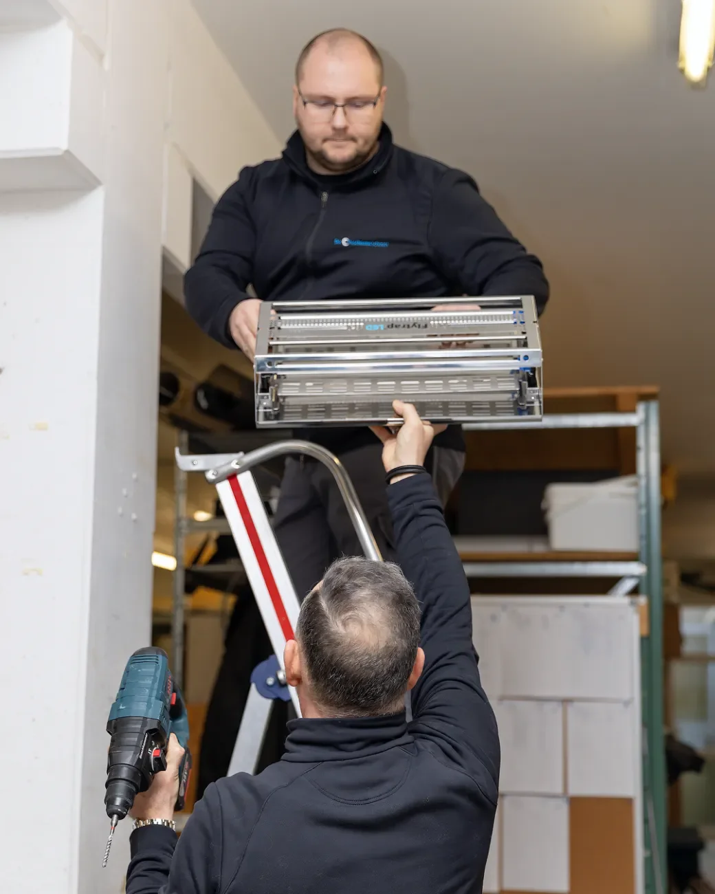 Ein Schädlingsbekämpfer montiert eine Fliegenfalle mithilfe eines Kollegen